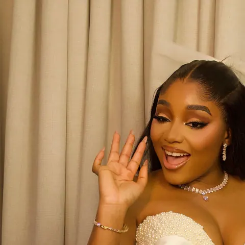 Kiky, the bride, waving at her surprise bridal shower in an ivory sculptural gown with a sheer bow headpiece