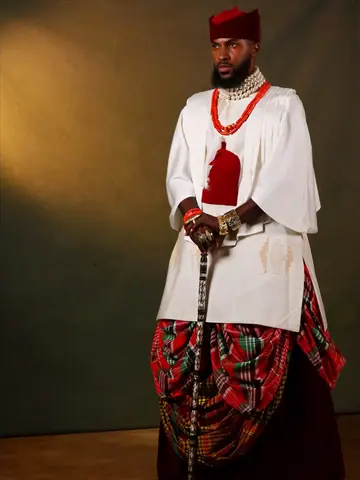 The groom in a white Igbo top, red cap and coral beads, holding a cane