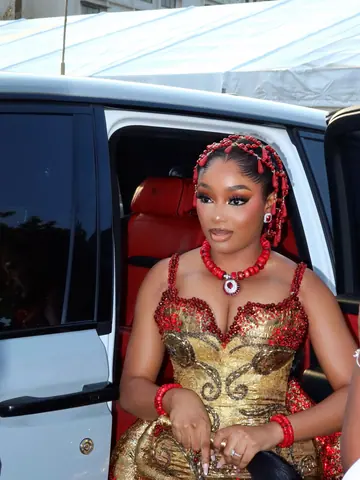 A bride stepping out of a white car in a gold-and-red gown with coral beads